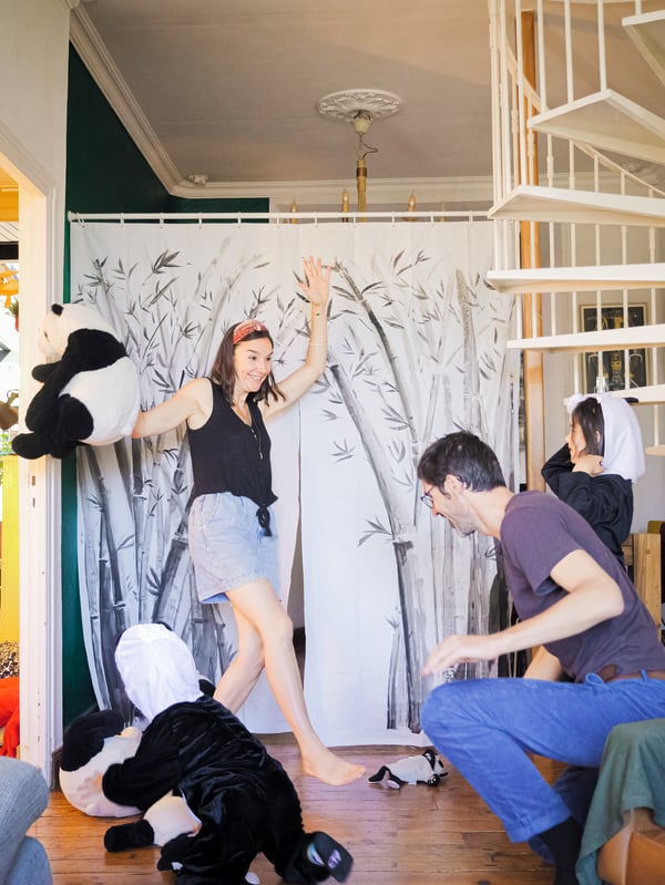 A mother, a father and two children in panda bear costumes perform a show in front of a 
stage curtain made from a decorated BJÄRSEN shower curtain.