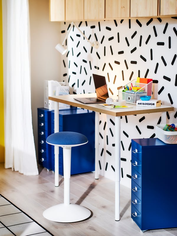 A colourful room with a workspace flanked by two blue HELMER drawer units on castors and a NILSERIK standing support.