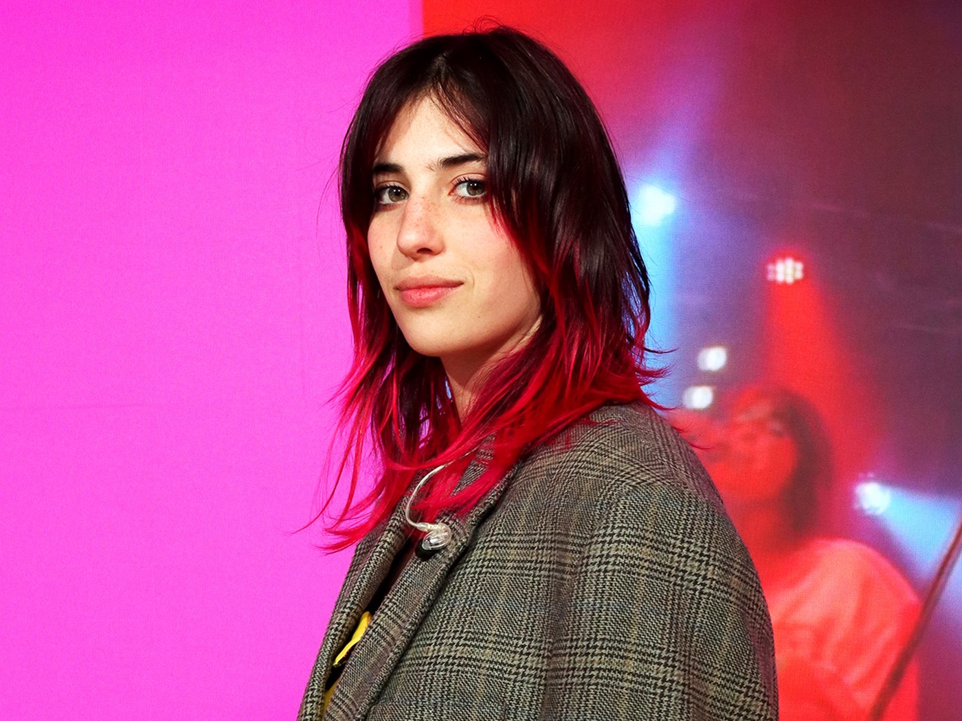 Chiamamifaro standing on a stage with a pink colour as a background that comes from the digital display used on stage during Milan design week 2024 at the IKEA venue.