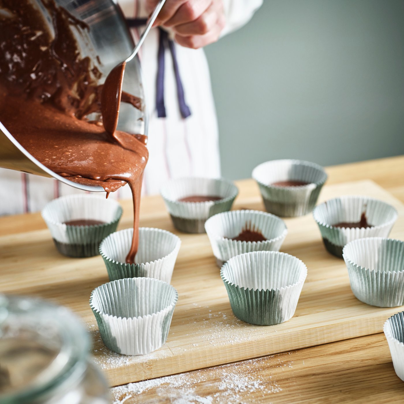 A person filling IKEA KRUSTISTEL baking cups with a chocolate batter.