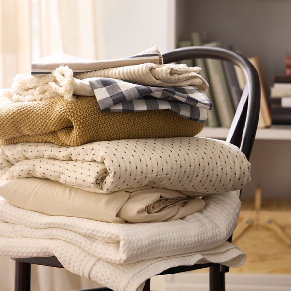 A pile of folded textiles in beige, white and yellow on top of SKOGSBO chair in dark brown.