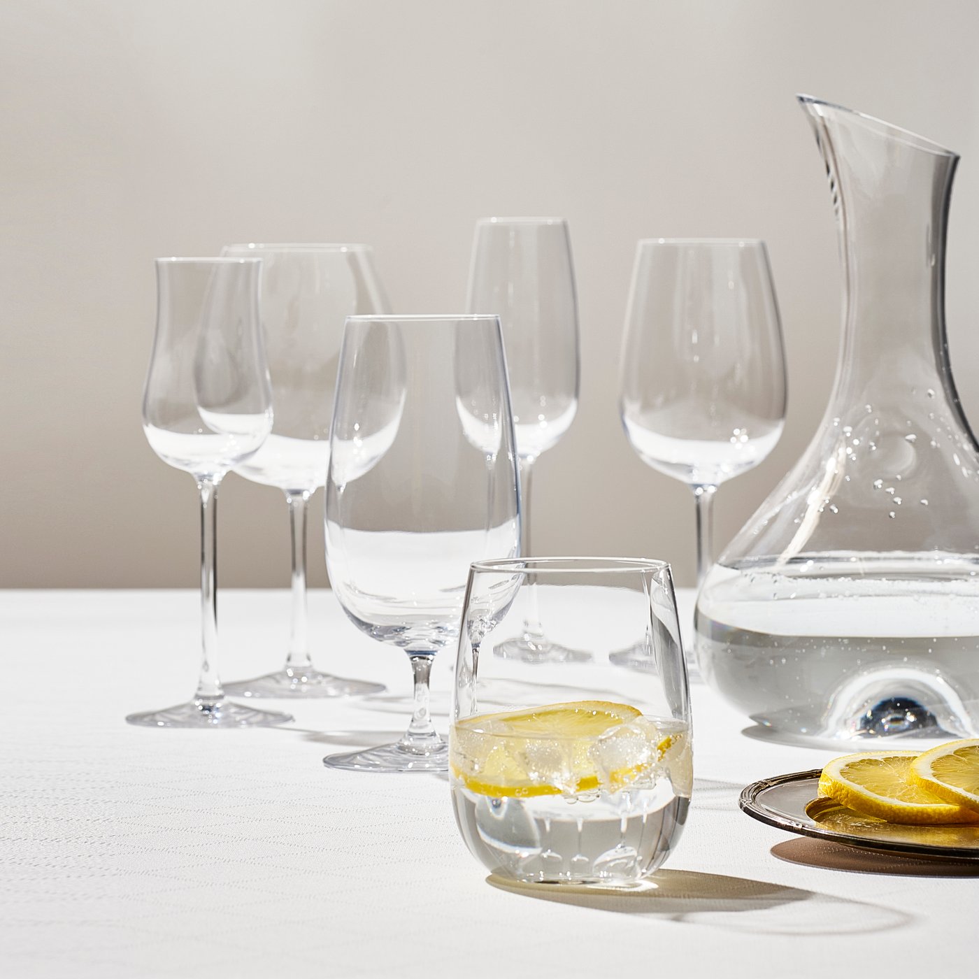 An assortment of IKEA STORSINT glasses in various sizes, a matching carafe on the side, on a white background.