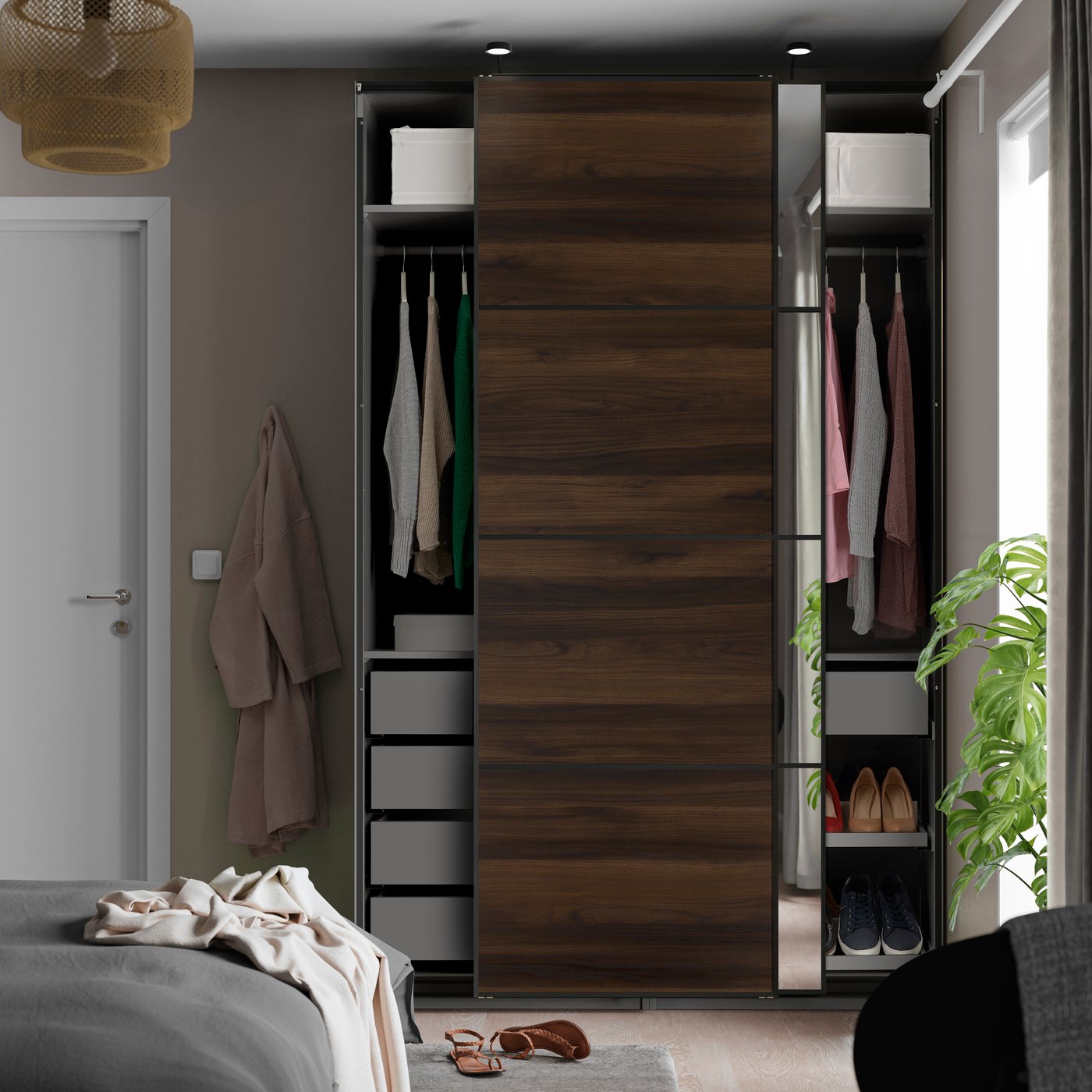 Une armoire-penderie PAX gris foncé effet chêne brun foncé/noir avec portes coulissantes en verre miroir dans une chambre.