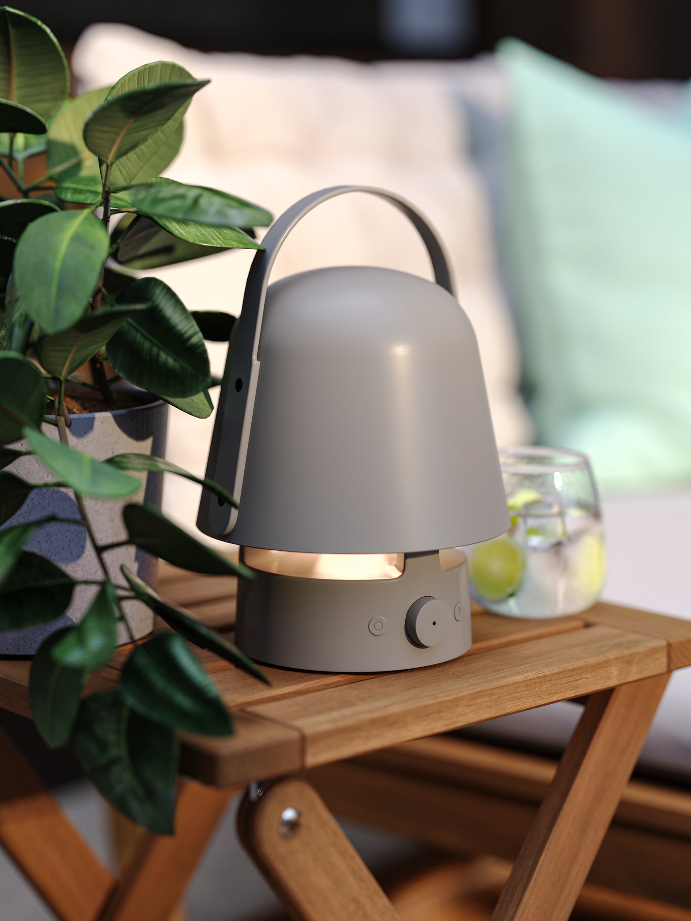 En loungezon på en uteplats med en grå VAPPEBY Bluetooth-högtalarlampa för utomhusbruk på en NÄMMARÖ akaciapall bredvid en växt.



