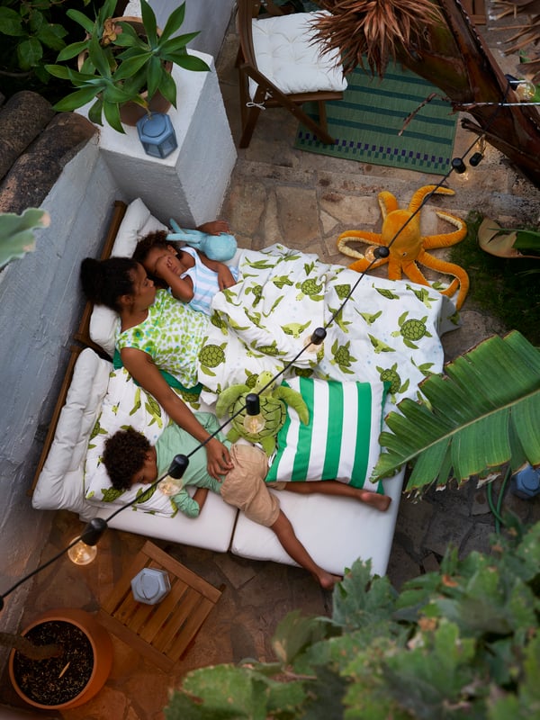 An adult and two children lying down on a NÄMMARÖ 2-seat sofa with two seat sections in an outdoor space.