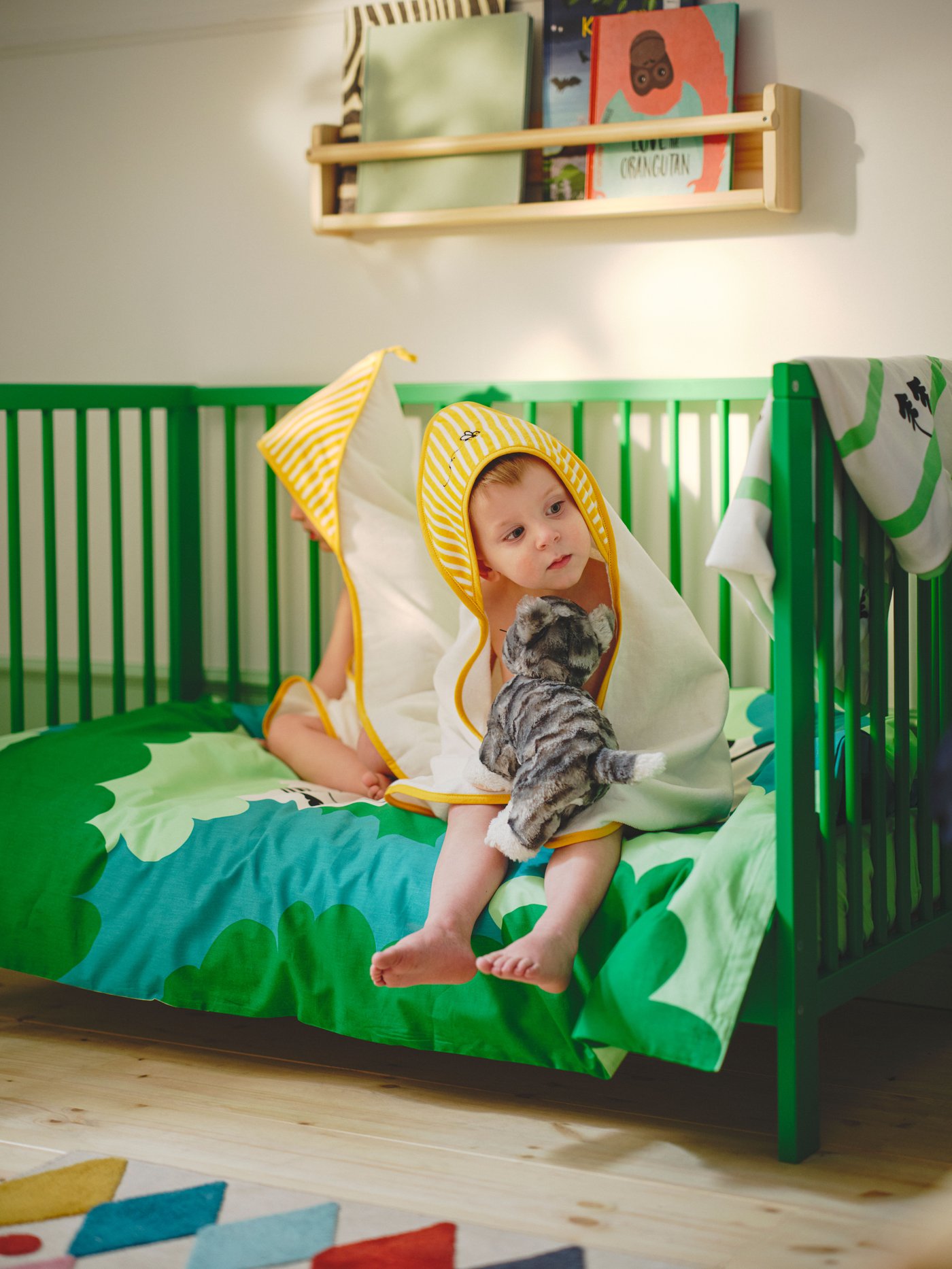 Zwei Kinder in gelben GRÖNFINK-Babyhandtüchern sitzen auf einem grünen GULLIVER-Kinderbett mit grün-türkisfarbener GRÖNFINK-Bettwäsche.