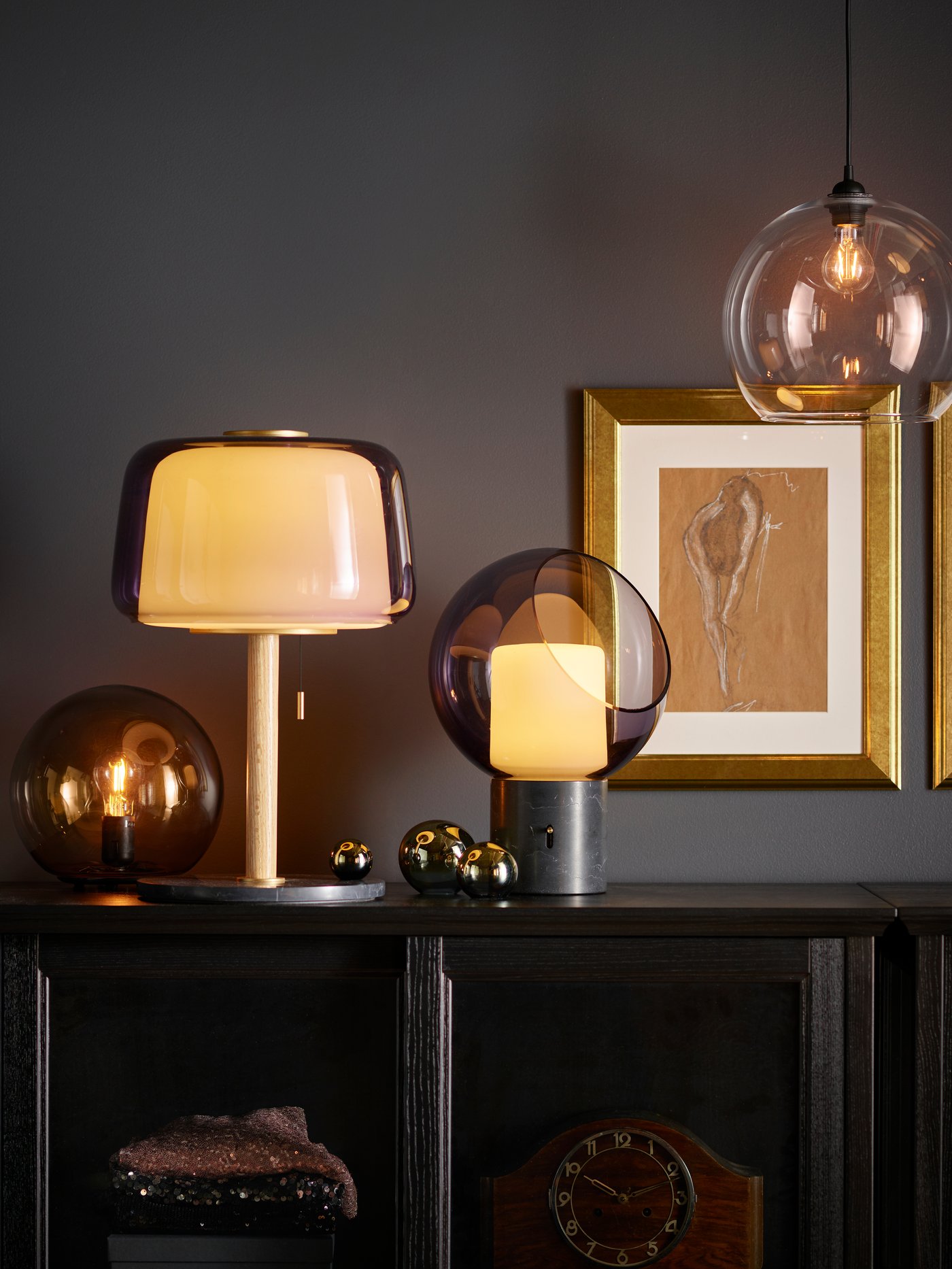 EVEDAL table lamp on top of a BESTA storage cabinet cupboard next to a FADO lamp. next to a few picture frames which are mounted on the wall. 