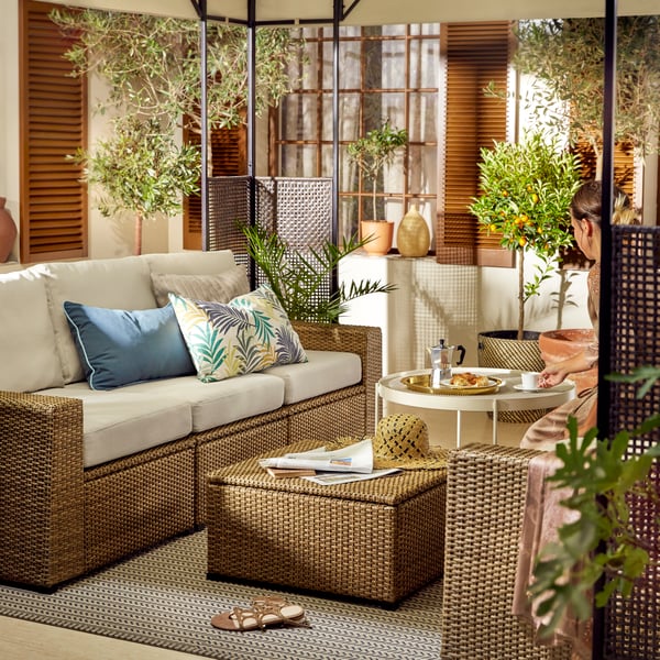 SOLLERÖN plastic rattan indoor and outdoor modular sofa in outdoor area with a outdoor rug in the middle and coloured cushions on top.