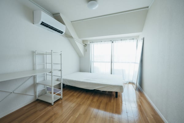 奥に白いベッド、左の壁際に白いラックが置かれている。