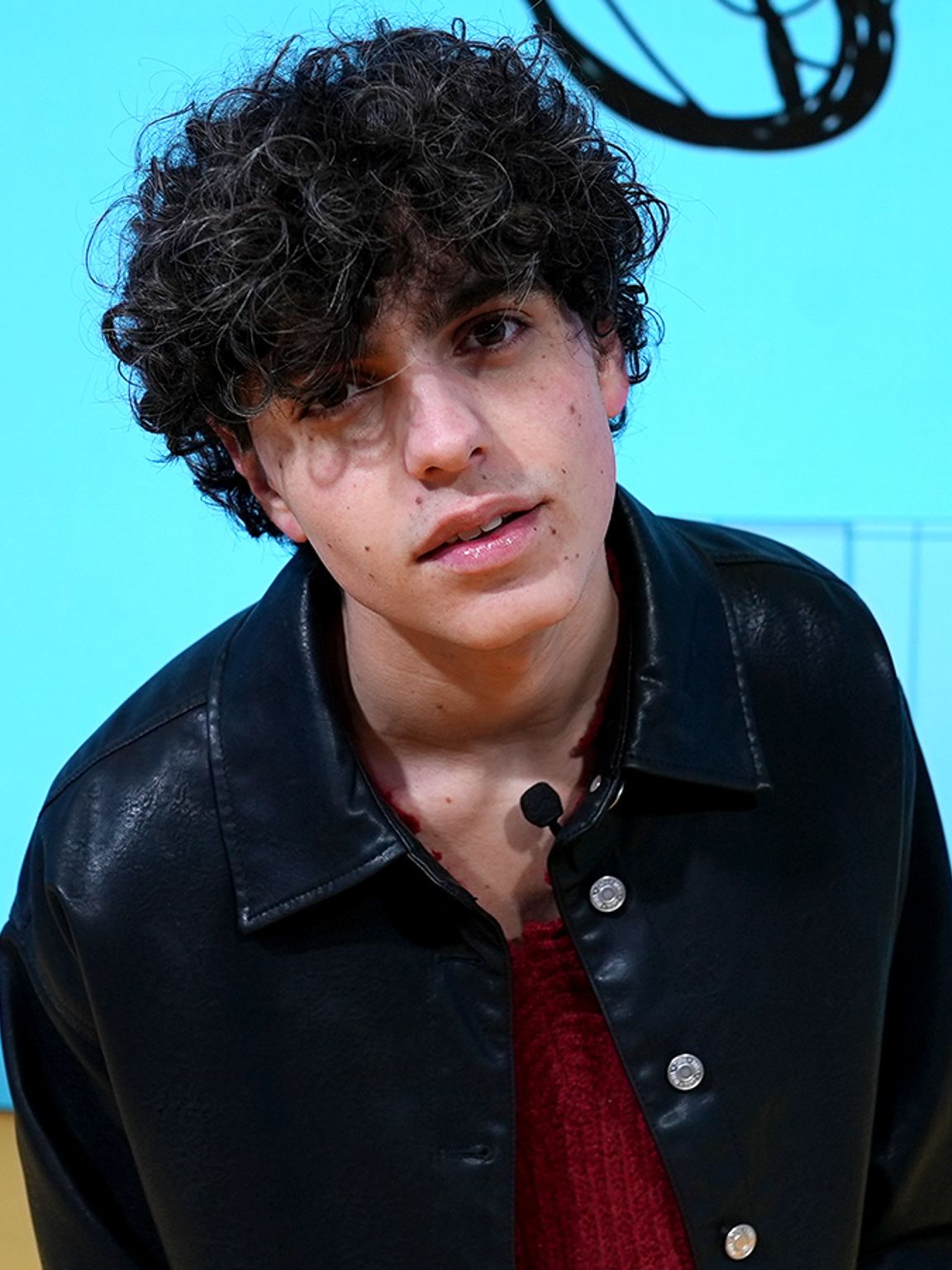 Niveo staat op het podium in een zwart shirt en met halsketting om, met op de achtergrond een blauwe kleur en enkele IKEA producten, afkomstig van de digitale display die tijdens de designweek in Milaan editie 2024 werd gebruikt in het IKEA paviljoen. 