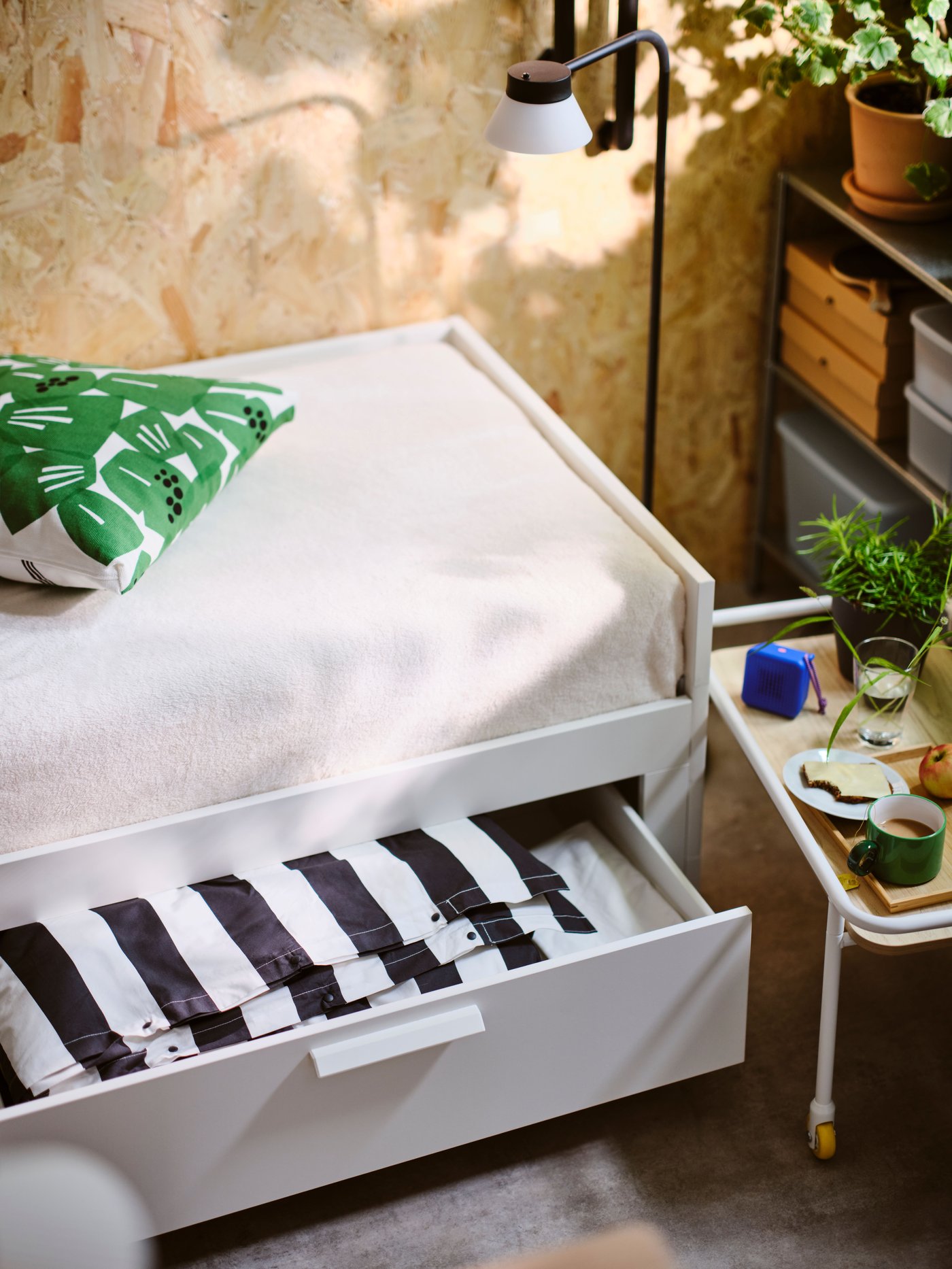 Un tiroir ouvert d'un lit de jour BRIMNES blanc à deux tiroirs, dans lequel on aperçoit du linge de lit SLÅNHÖSTMAL rayé noir et blanc, soigneusement plié.