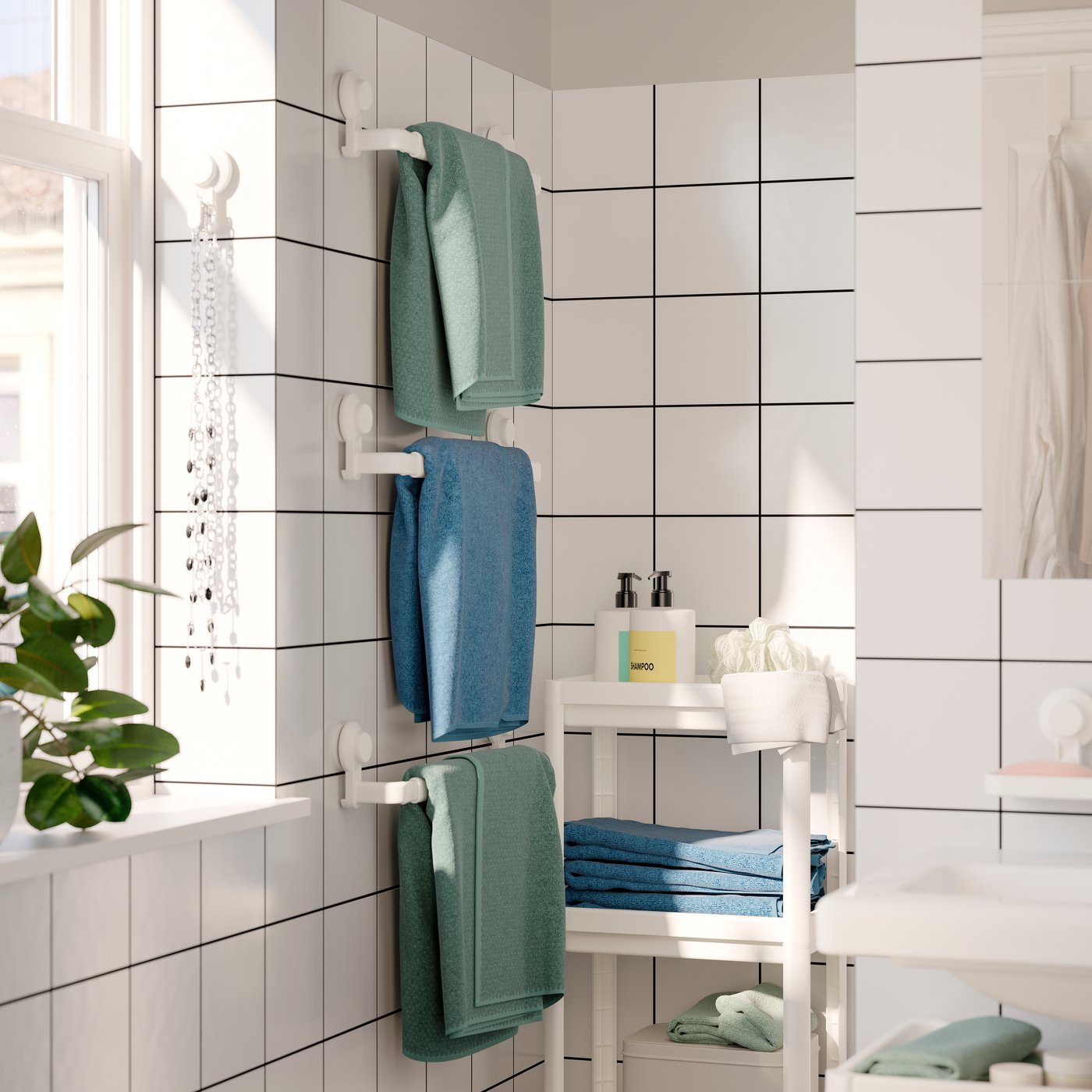 Three bath towels in muted green and blue hanging from three TISKEN towel racks with suction cup. White tiled bathroom.