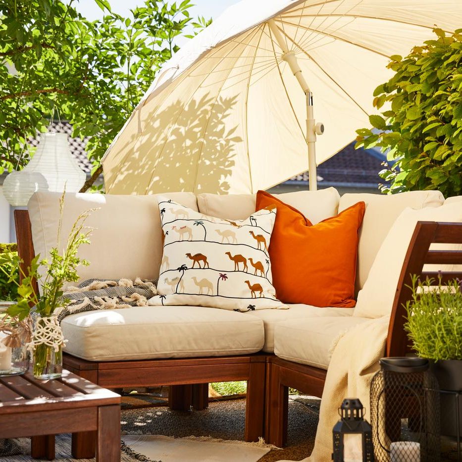Gemütliche Outdoor-Sitzecke mit weissen Polstern, Zierkissen, Holzmöbeln und Sonnenschirm im grünen Garten.