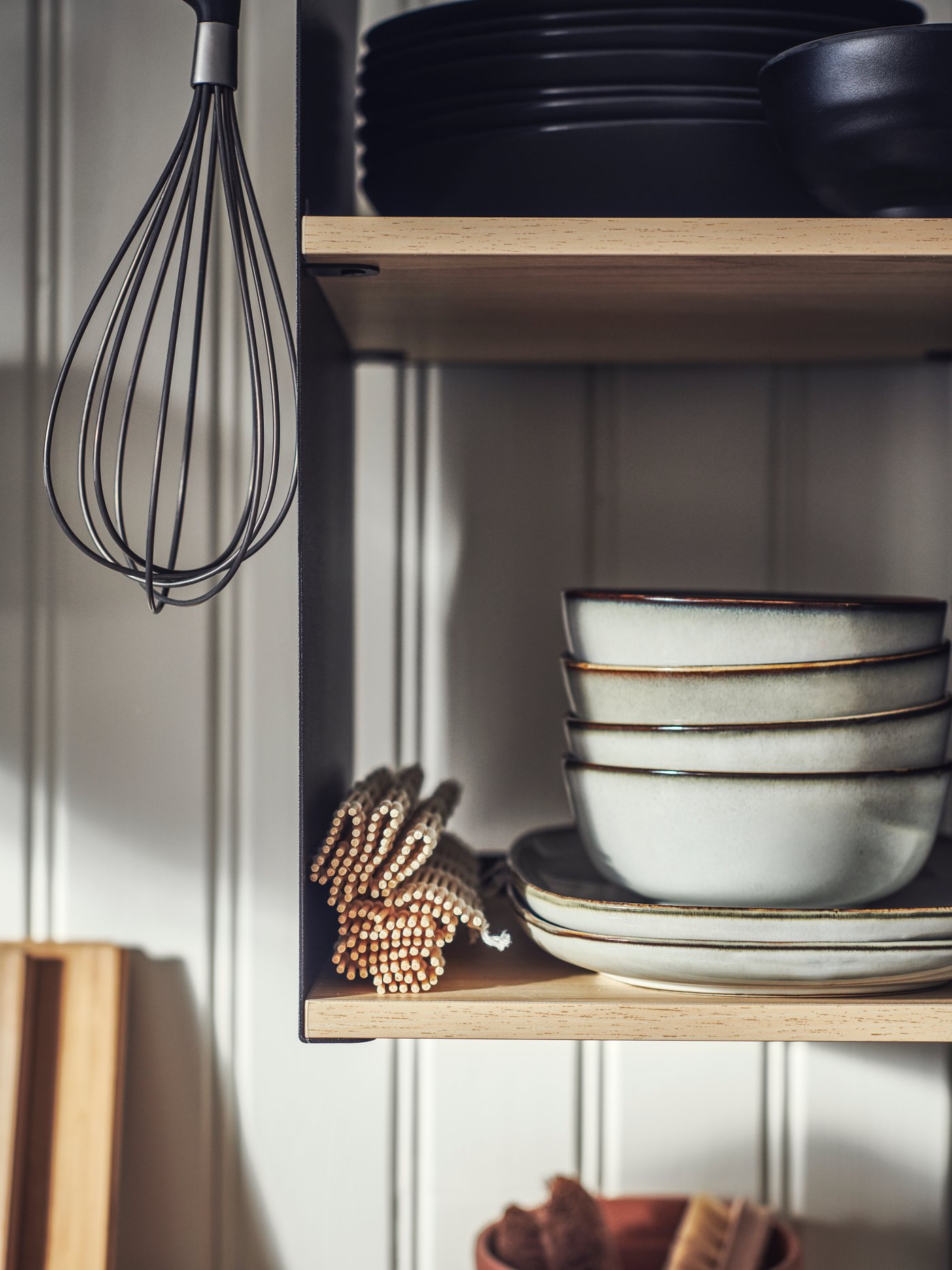 The shelves of an ÄSPINGE kitchenette holding GLADELIG side plates and bowls in grey and FÄRGKLAR plates in matte dark grey.
