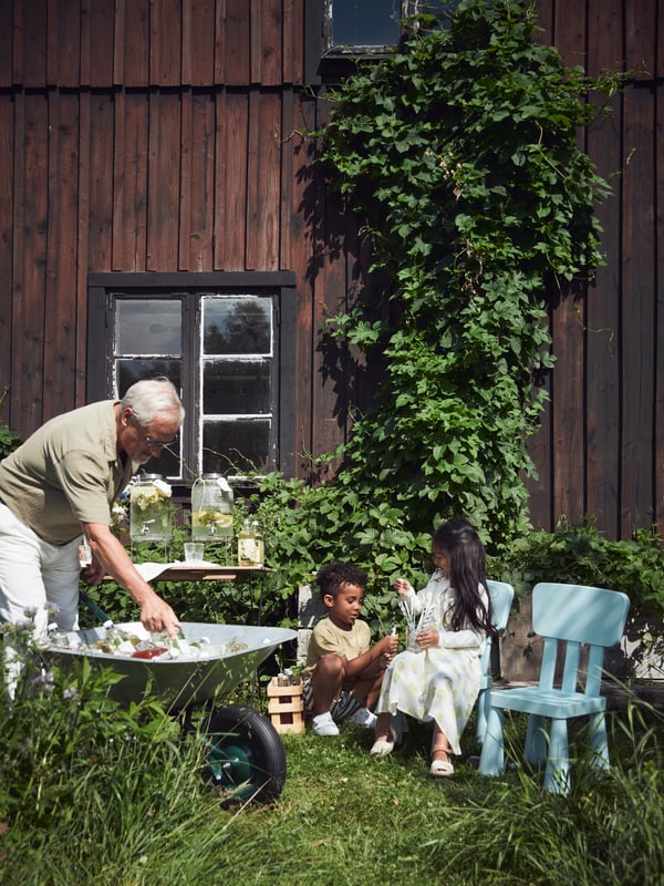 Two kids enjoy a midsummer party on MAMMUT chairs, chatting in the garden while waiting for grandpa to serve drinks.