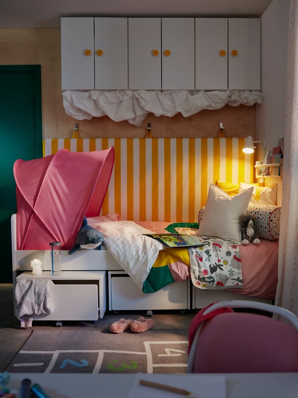 A child’s room with a SLÄKT bed and storage boxes with a FUBBLA wall lamp at one end, and a SUFFLETT bed tent at the other.