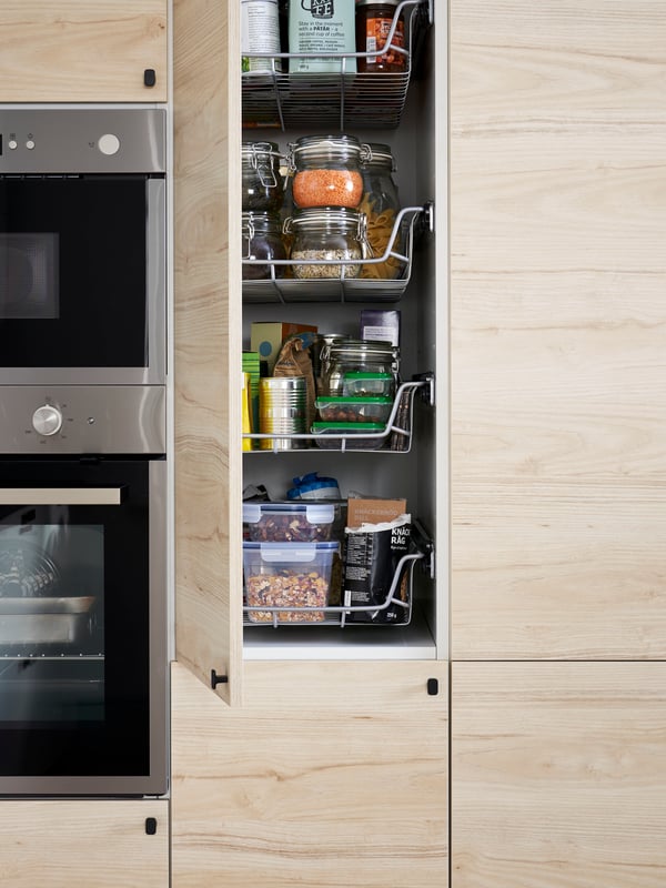 A tall cabinet in a kitchen with an open light ash effect door showing wire baskets, food containers and more.