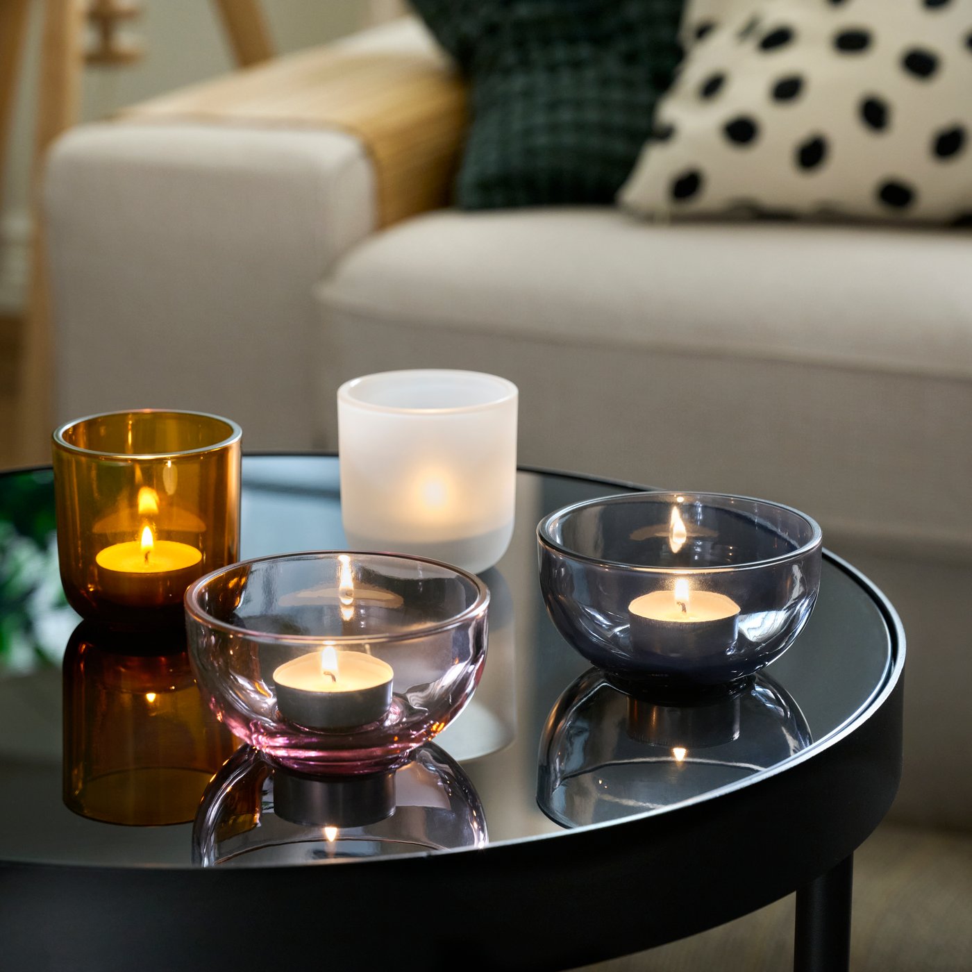 Two TALLTITA tealight holders, separated to form four individual parts, each with a lit tealight, set on a round side table.