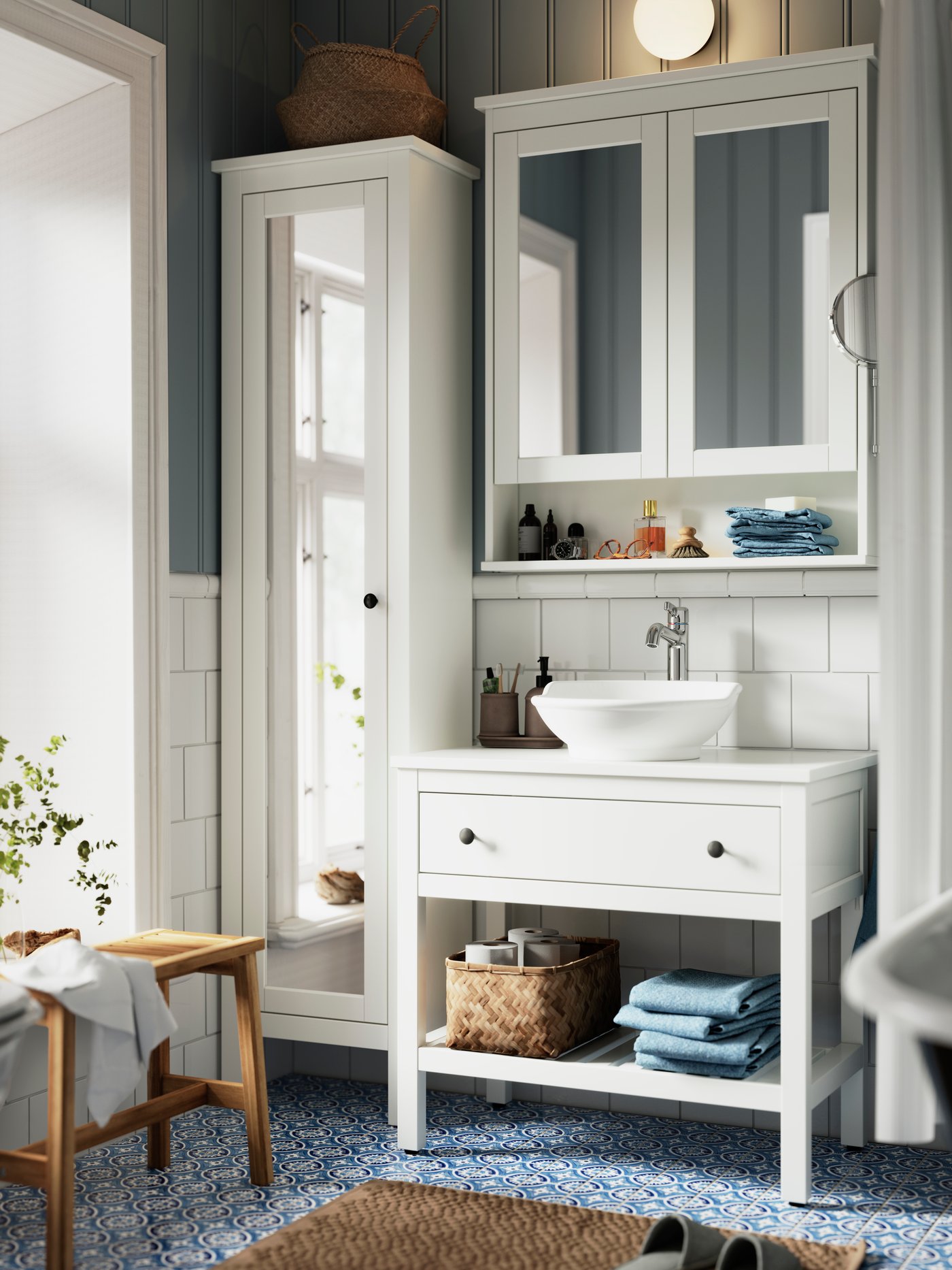 Modrobílá koupelna s modrou dlažbou má bílý koupelnový nábytek HEMNES a lavici STOREDAMM vyrobenou z akácie.