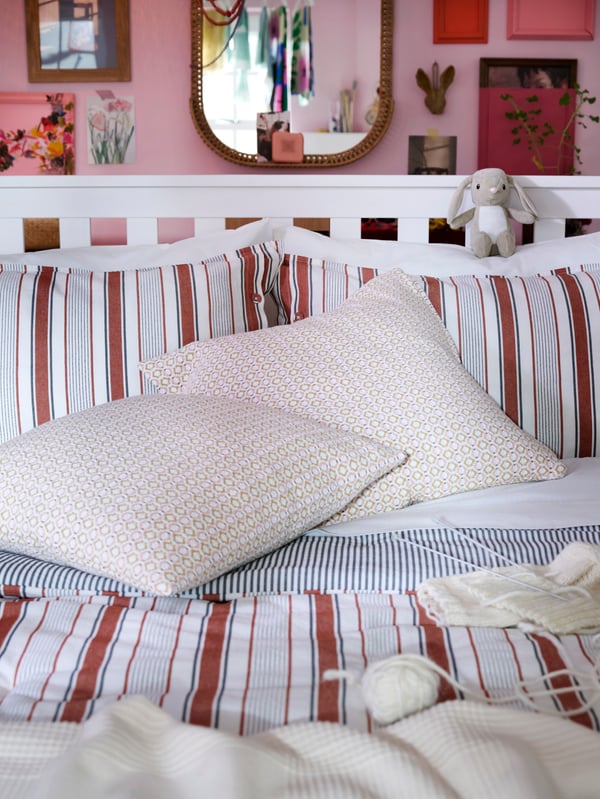 Close-up of white HEMNES bed with GULDAKLEJA bedding and extra cushions in light pink.
