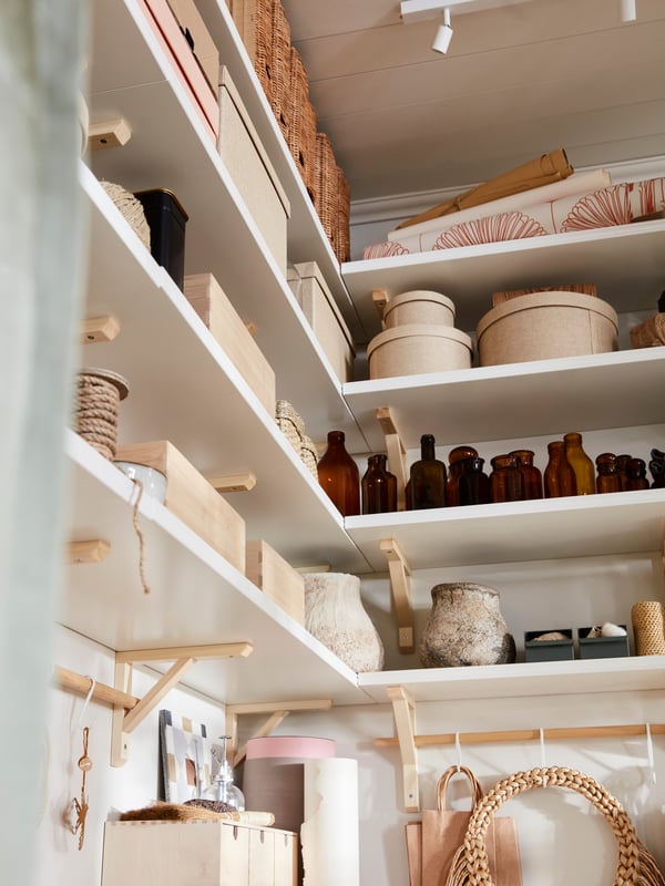 A tall storage space with white BERGSHULT wall shelves reaching up to the ceiling, holding various small storage boxes and personal items.