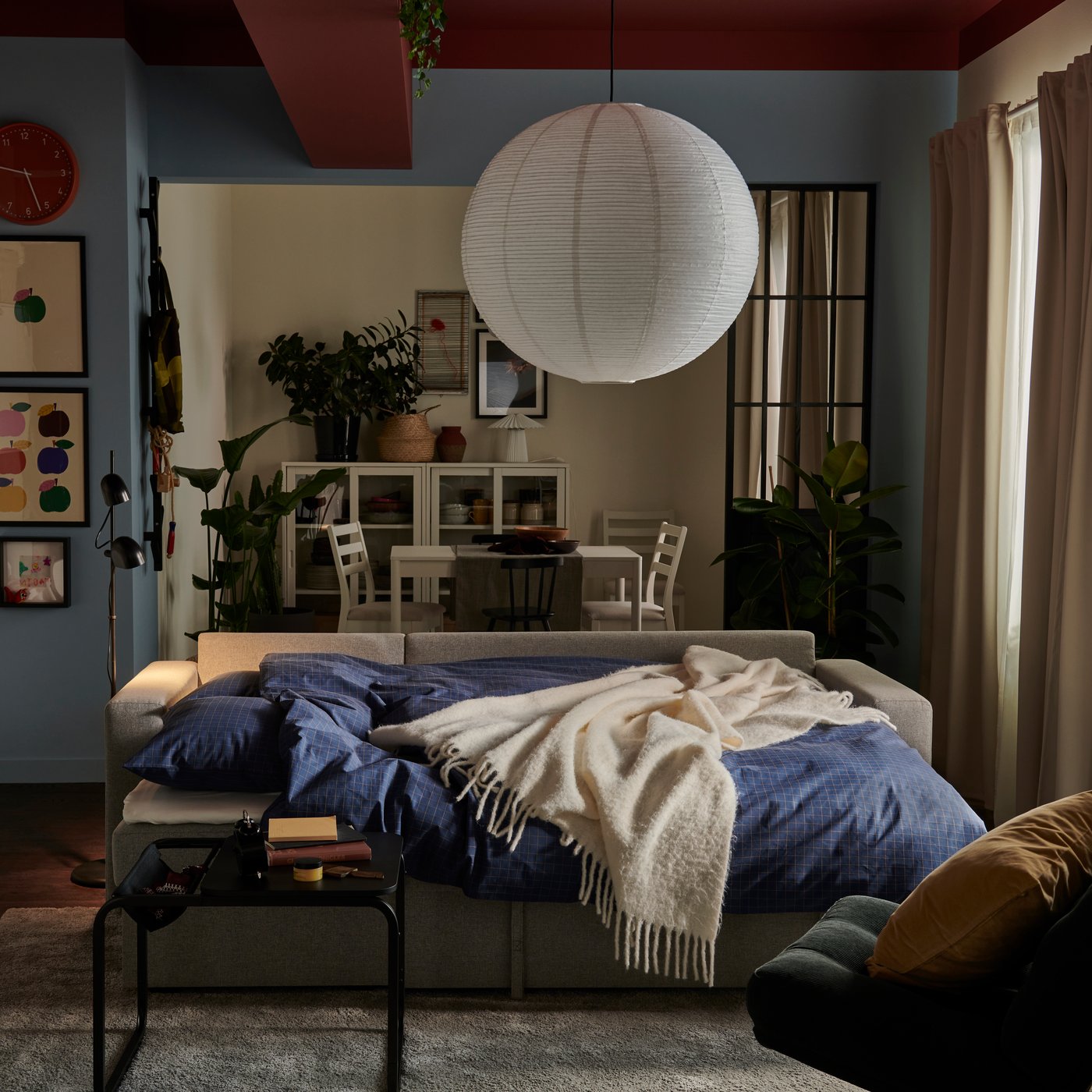 En beige/grå BÅRSLÖV 3-personers sovesofa med chaiselong i en lys stue dekoreret med planter og en stor rispapirslampe i midten af rummet.
