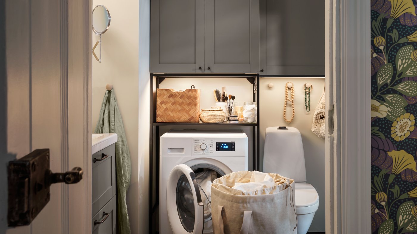 A bathroom laundry, storage with ENHET fronts in grey, an UDDARP washer/dryer combination and a PURRPINGLA laundry bag.