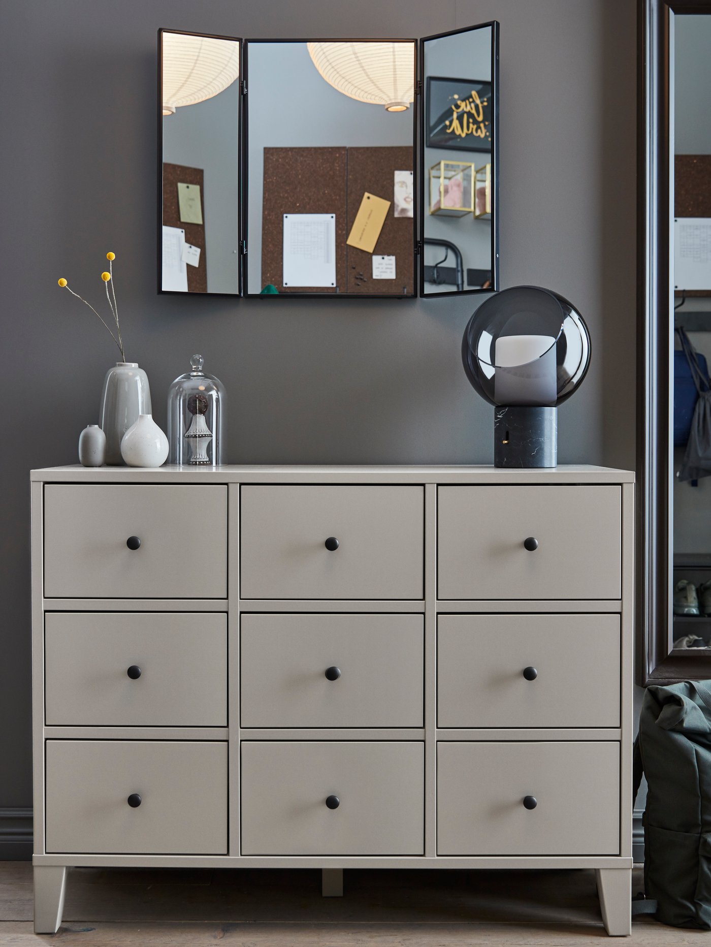 A BRYGGJA chest of drawers with a KARMSUND mirror on the wall above, and with vases and an EVEDAL table lamp on top.