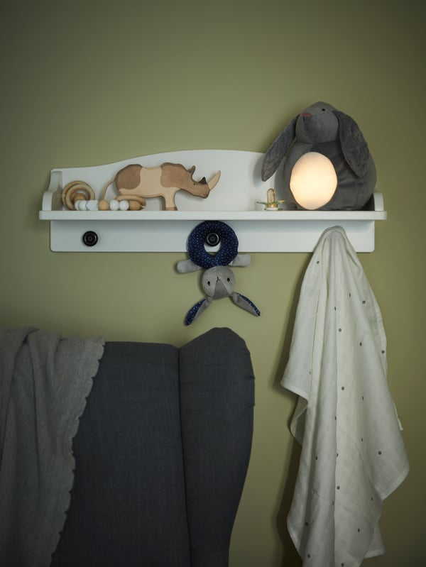 A white wall shelf, wooden toys, grey rabbit/battery-operated soft toy with LED night light, a dotted muslin square.