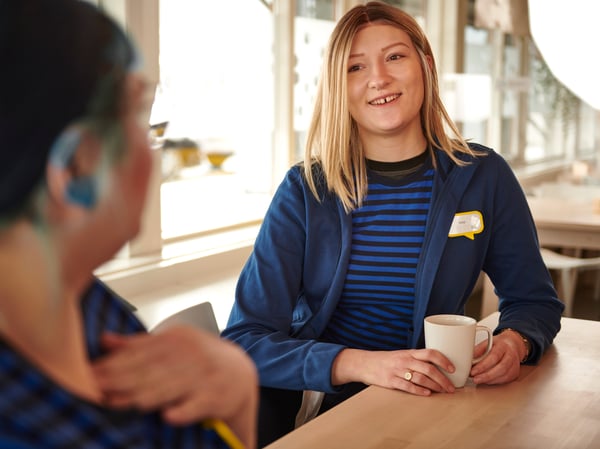 To IKEA medarbejdere i blå uniformer nyder en pause i medarbejderkantinen.