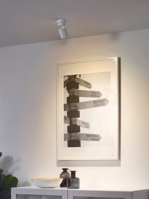 En NYMÅNE lysspot med et spot er monteret i loftet og lyser på en plakat på en væg.