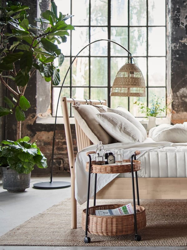 A bedroom with a carpet, a lampshade and a bed in natural materials.
