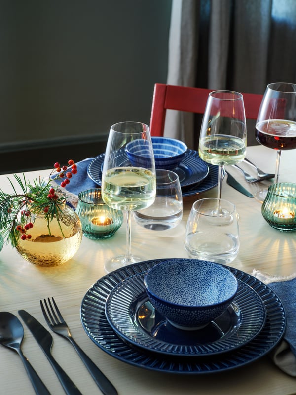 Una mesa decorada con ramitas de pino. Los platos STRIMMIG de color azul están montados desde el más grande al más pequeño uno sobre otro.