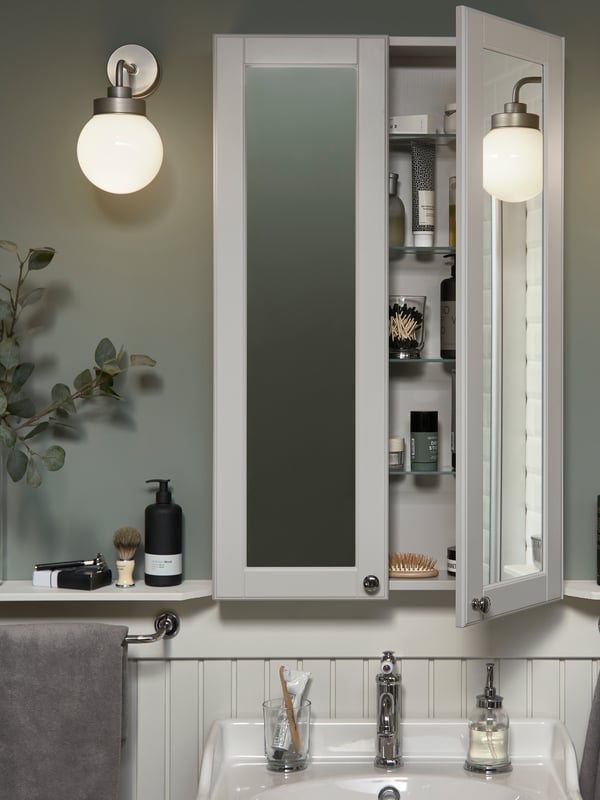 A shallow but high mirror cabinet over a white wash-basin. One door is open, and beauty items are stored inside.