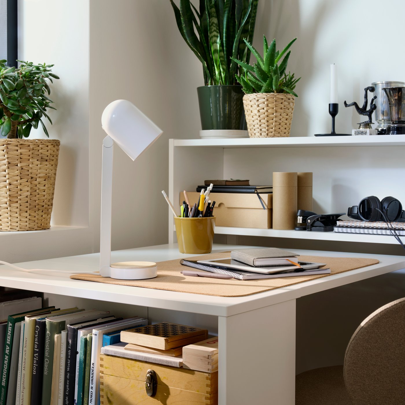 A corner of a bright room with a BILLY bookcase pulled out to form a desk, with an ENSMÄRKE lamp and desk accessories on it.