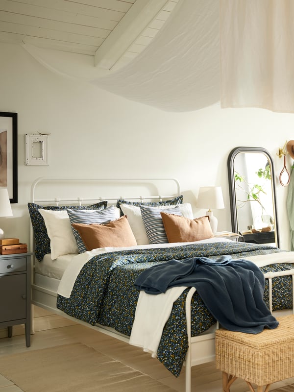 A white STJÄRNÖ bed covered in a ROSENTIBAST comforter set and a white INDIRA bedspread and various cushions.