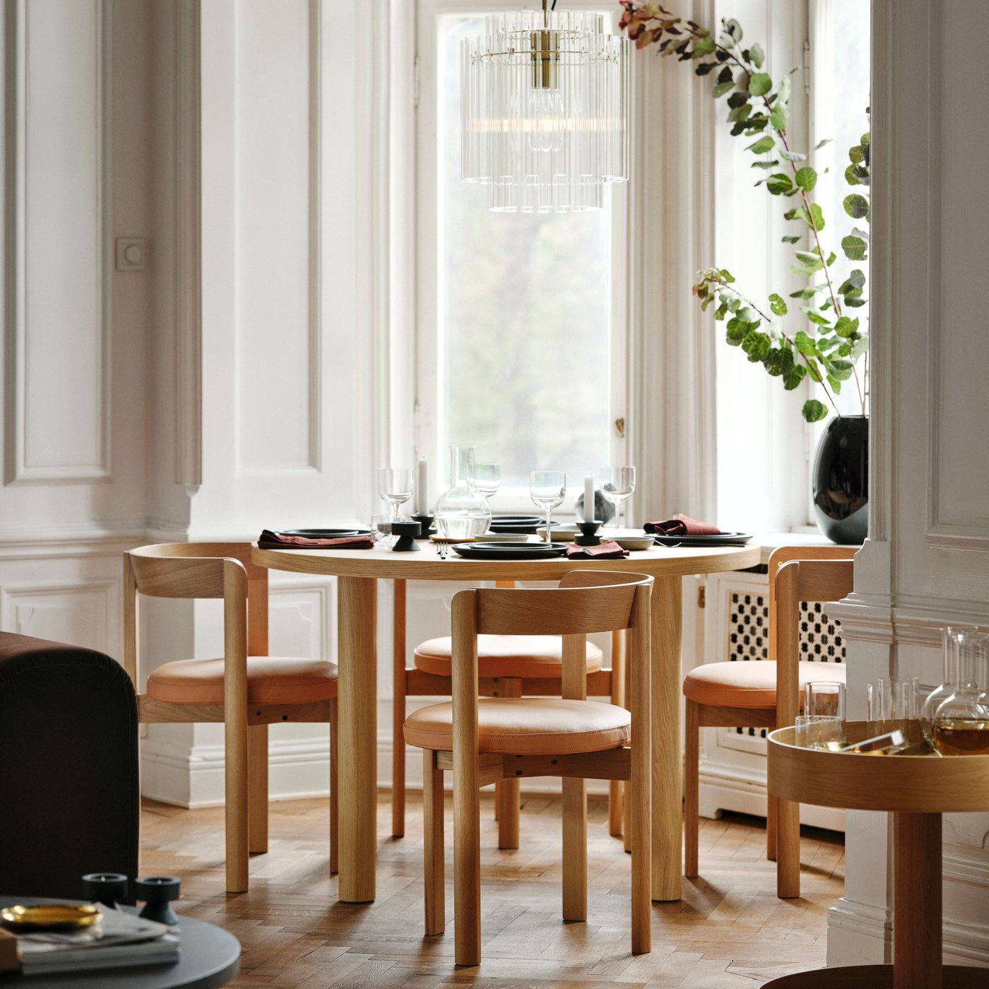 Four STOCKHOLM 2025 oak chairs with leather seats around an oak veneer table by a living room window.