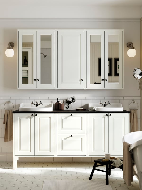 White TÄNNFORSEN cabinets with two sinks and two mirror cabinets with black knobs are mounted in a white bathroom.