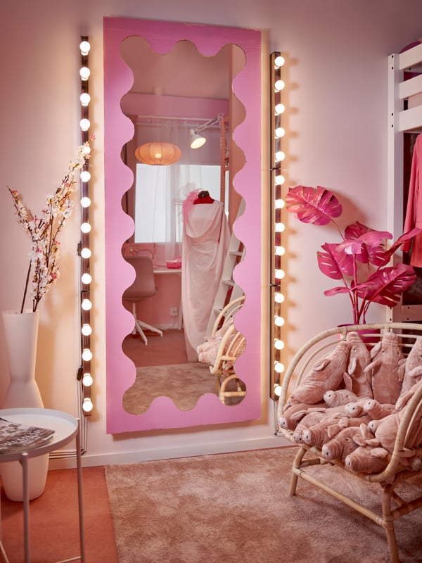 A mirror with a pink cardboard on it to create a shape with waves around. Around the mirror are festoon lights.