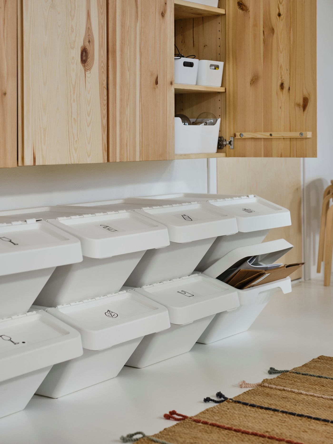 Rows of white SORTERA waste sorting bins with lids on top of one another under two pine IVAR cabinets with one door open.