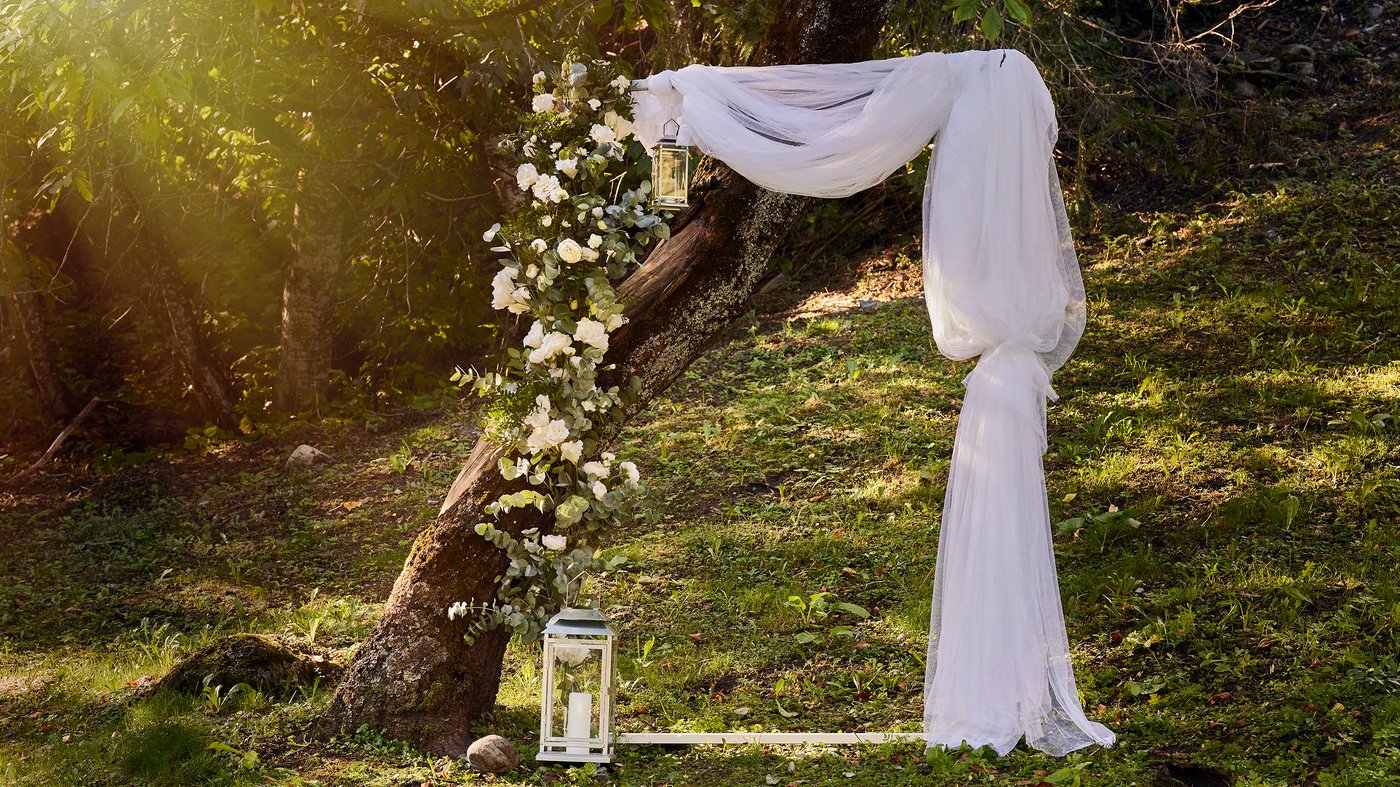 Ett egengjort fotobås med en stor fotoram dekorerad med LILL tyllgardin och SMYCKA blommor står i naturen.