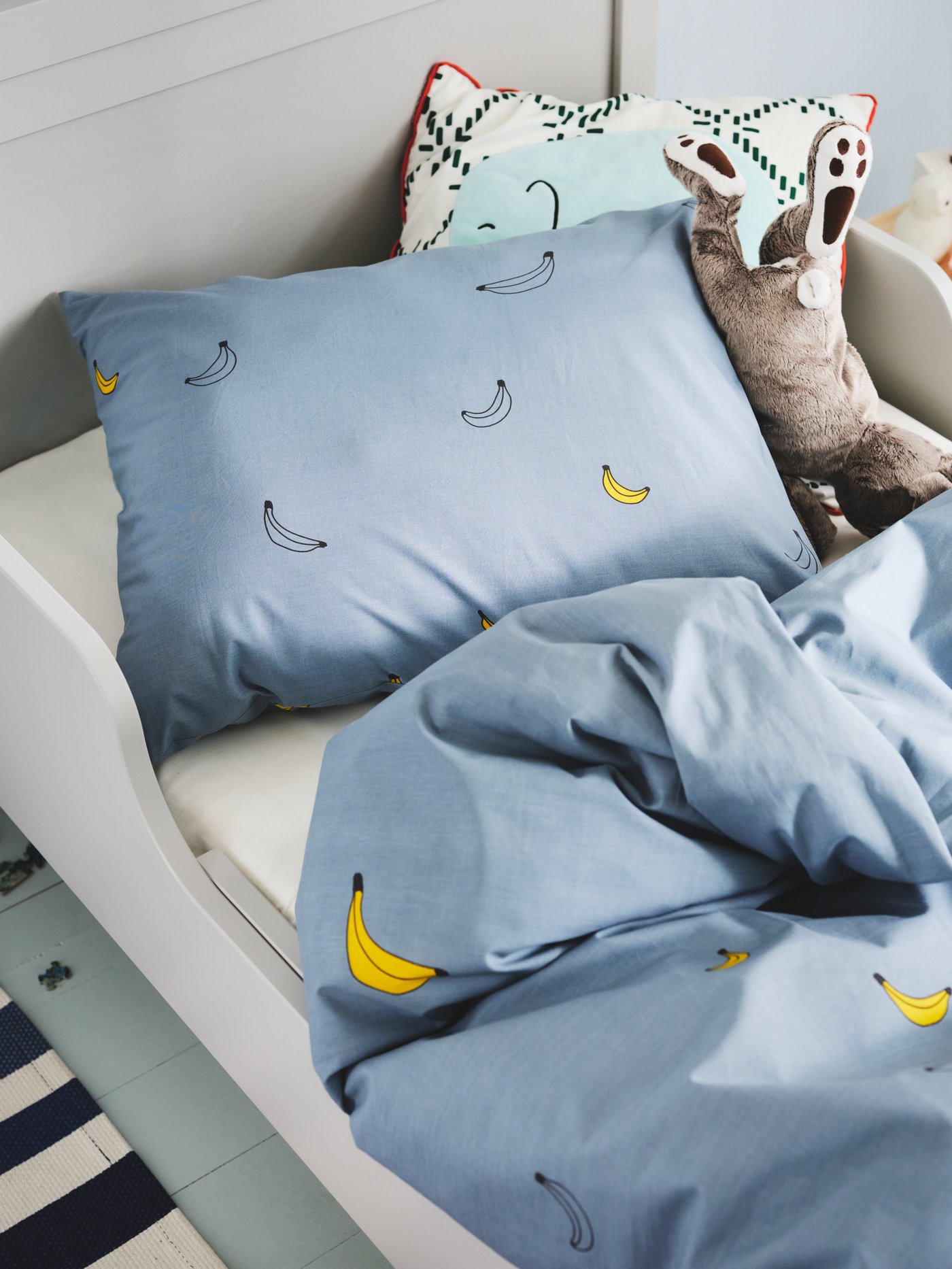Ein Kinderzimmer mit ausziehbarem Bettgestell und einem VÄNKRETS Bettwäscheset in Blau mit Bananenmuster.