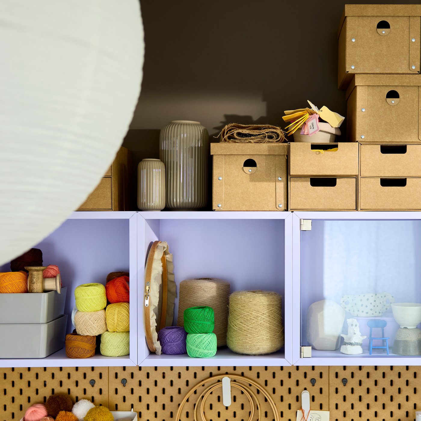 Närbild av ett EKET hyllsystem i ljuslila, fyllt med färgglada garner, pysselmaterial och förvaringslådor i olika storlekar.