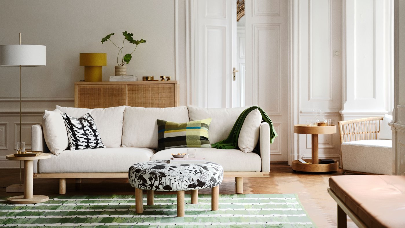 A living room with a STOCKHOLM 2025 3-seat sofa, pillows and a throw on it, and a black and white pouffe on a rug in front.