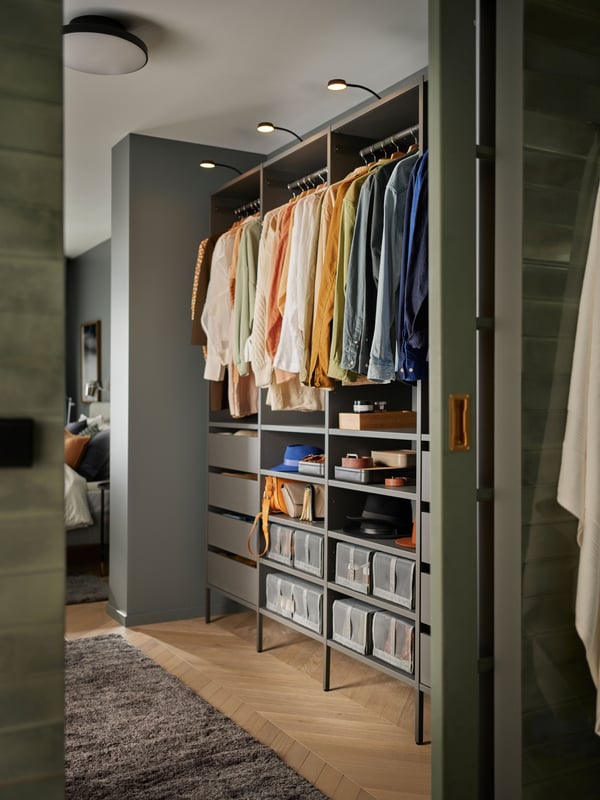 An open wardrobe combination in dark grey with both shelves, drawers, storage boxes and hanging clothes in perfect order.