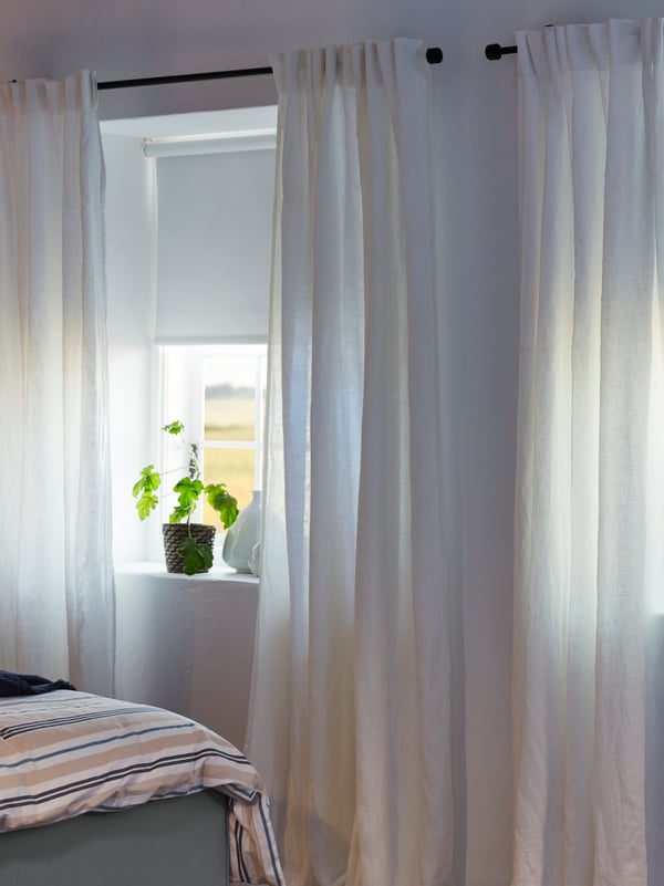 La ventana de un dormitorio con cortinas entollables FRIDANS y al costado cortinas de tela AINA.