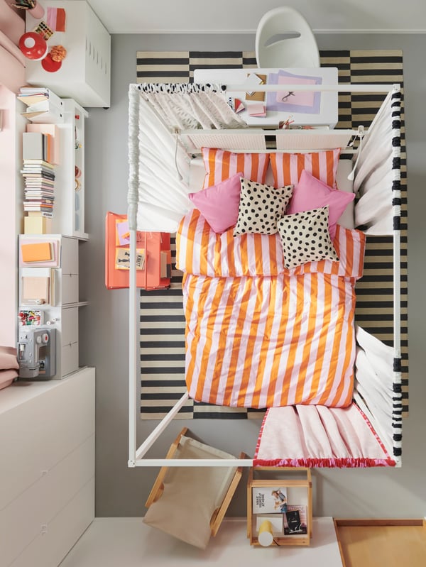 A top view of a bedroom with a VITARNA four-poster bed in the centre, covered with pink/orange SLÅNHÖSTMAL bed linen.
