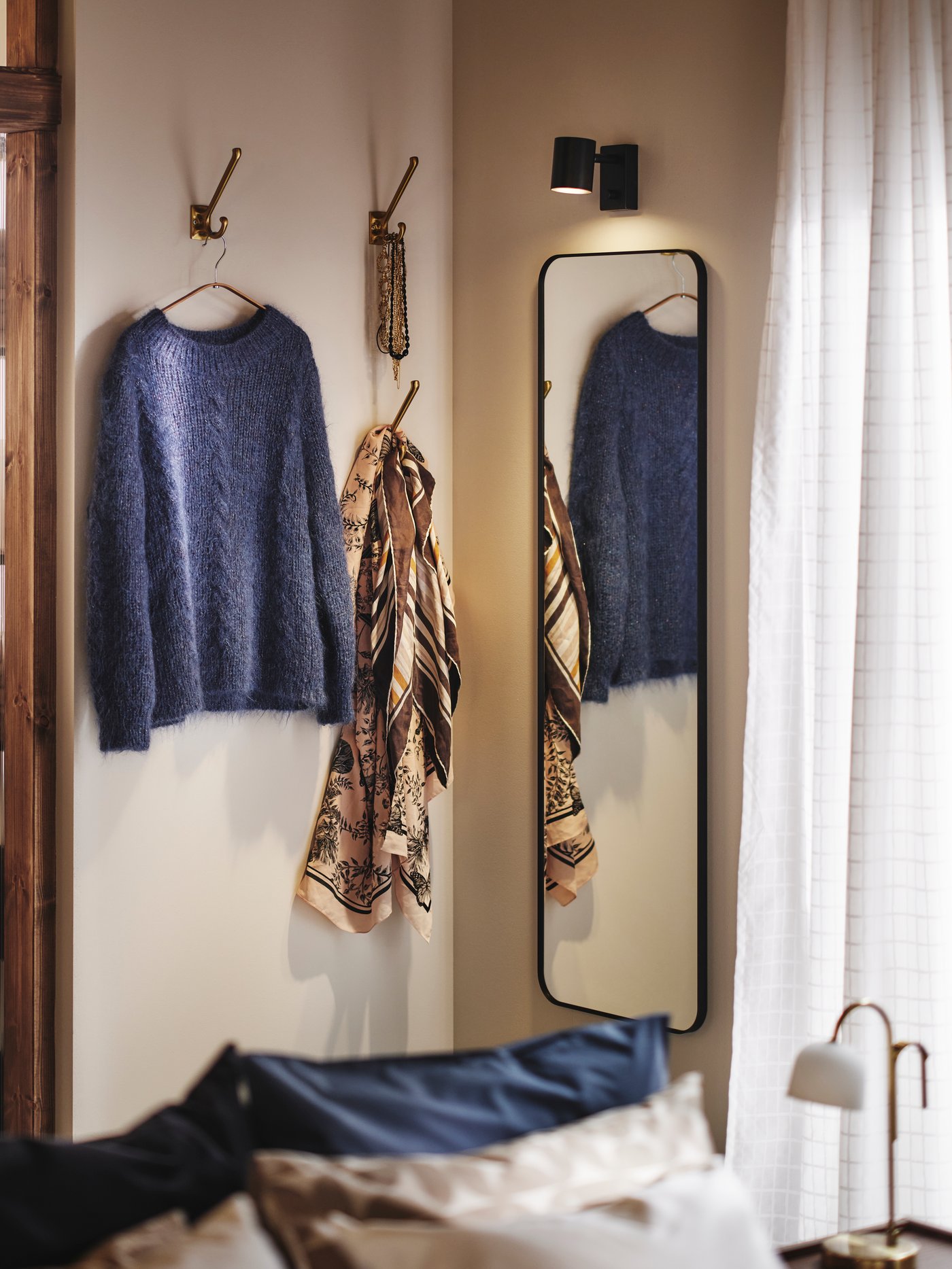 Corner of a bedroom with LINDBYN mirror and hooks for clothes and accessories on the walls. Glass doors and window at the sides.