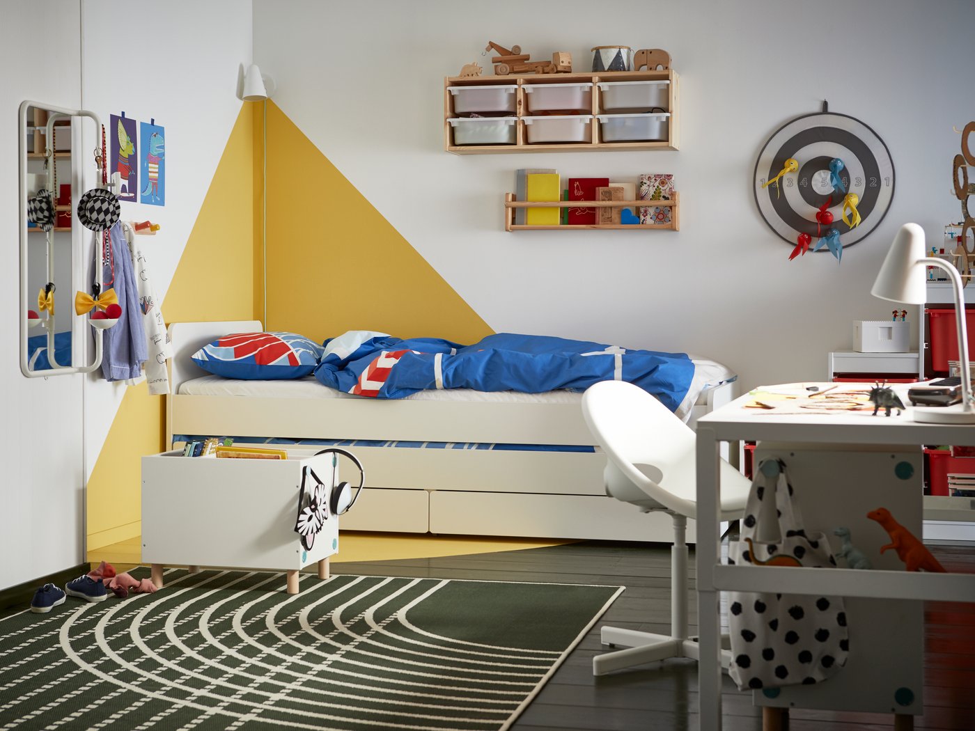 A children's bedroom with graphic white and yellow walls, a white bed with storage underneath, blue and red bed linen.