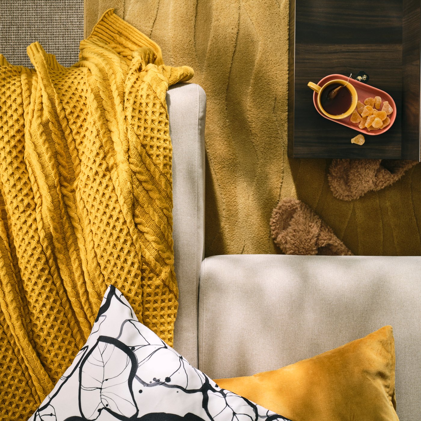 A corner of a light-beige MALMKÖPING sofa with textiles and coffee accessories coordinated in a mustard-yellow colour scheme.